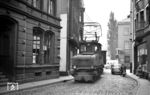 E-Lok 7 (AEG, Baujahr 1926) ist mit einem Rollwagenzug vom Betriebshof der Linscheidstraße in Altena kommend in die Bachstraße Richtung Nette eingebogen und hat dabei die dort beginnende Lennestraße (im Hintergrund links) und die Straße Iserlohner Berg (auf der rechten Seite) hinter sich gelassen. Es ist nicht verwunderlich, dass es hier heute völlig anders aussieht, da u.a. die Straße durch Abriss von Gebäuden aufgeweitet wurde. (24.09.1959) <i>Foto: Aad van Ooy</i>