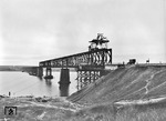 In den letzten Zügen des Wiederaufbaus befindet sich diese ein Kilometer lange Eisenbahnbrücke über den südlichen Bug bei Trichaty (Trykhaty) an der Bahnstrecke Nikolajew (Mykolajiw) - Kolosowka (-Odessa). Der Bohlenpfad am Hang ist Teil der Brückenwache. Die Brücke ist heute noch eingezäunt und wird nach wie vor bewacht! (1943) <i>Foto: Walter Hollnagel</i>