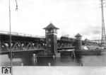 Eine unbekannte 64 passiert die Eisenbahnbrücke über den Pregel am Holländerbaum in Königsberg/Ostpreußen. Sie wurde 1926 als doppelstöckige Drehbrücke errichtet. Der obere Teil diente dem Schienenverkehr, der untere dem Straßenverkehr. Im aufgedrehten Zustand gab die Brücke zwei Schiffsdurchfahrten von je 17,5 Metern frei. Die Brücke  wurde im 2. Weltkrieg stark beschädigt und danach als Hebebrücke wieder aufgebaut. (1932) <i>Foto: RVM</i>