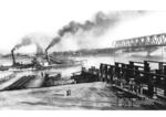 1865 wurde erstmalig in Europa eine gemeinsame Eisenbahn- und Straßenbrücke als Schiffsbrücke über den Rhein bei Karlsruhe ausgeführt.Die Schwimmbrücke von Maxau hatte eine Gesamtlänge von 363 m, wovon 234 m auf die eigentliche Flußüberquerung und 129 m auf die beiden Zufahrtsrampen entfiel. Sie bestand aus 34 Pontons, auf denen 12 Fahrbahnjoche montiert waren. Sechs der Fahrbahnjoche konnten für die Durchfahrt von Schiffen geöffnet werden. Rechts ist die 160m stromaufwärts befindliche neue feste Brücke zu erkennen. (1937) <i>Foto: RVM</i>