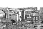 Zunächst gab es über die Schwarzbach in Wuppertal-Oberbarmen eine Gitterbrücke in sog. Fischbauchträger-Bauart (siehe Bild-Nr. 50472). Kurze Zeit nach der Eröffnung wurde bereits eine verstärkte Konstruktion aus Stahlträgern eingesetzt, die 1980/81 durch eine neue Brücke ausgetauscht wurde. Deutlich erkennbar ist die Tatsache, wie nahe der Fahrweg der Verbindung zwischen Rittershausen (Oberbarmen) und Wichlinghausen an den Häusern mit der engen Bebauung entlang verlief. Die Gegend war altes Industrie- und innerstädtisches Wohngebiet und wurde in alten Karten mit “Ober-Rittershausen” bezeichnet. Unter der Brücke fuhr ab 1874 zunächst eine Pferdebahn (mit Depot in der Schwarzbach), dann zwischen 1896 und 1987 gab es die Straßenbahn. Heute ist alles, was auf dem Bild zu sehen ist Geschichte. (1910) <i>Foto: RBD Wuppertal</i>