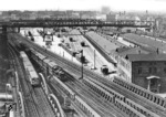 Ein dampfbespannter S-Bahnzug mit einer pr. T 12 in Richtung Potsdamer Ringbahnhof und ein Hochbahnzug begegnen sich in der Nähe des Potsdamer Güterbahnhofs (zum gleichnamigen Fernbahnhof gehörig). Ganz rechts ist die Abstellgruppe des Potsdamer Bahnhofs zu erkennen, wo ein langer Schnellzug abgestellt ist. Von links aus gesehen sind folgende Anlagen zu erkennen:- Hochbahnstrecke zum "U-Bahnhof" Gleisdreieck- Vorortbahnstrecke zum Bahnhof Yorckstraße- Südringspitzkehre zum Bahnhof Kolonnenstraße- Potsdamer Güterbahnhof mit Ladegleisen und Güterschuppen- erst nach dem Güterschuppen die Fernbahnstrecke / Stammbahn zum Bahnhof Zehlendorf (nicht direkt sichtbar)- Wannseebahnstrecke (ebenfalls nicht direkt sichtbar). Der heutige U-Bahnhof Mendelson-Bartholdy-Park befindet sich im Rücken des Photographen.Das heutige Parkhaus befindet sich über den Trassen der Vorortbahnstrecke zum Bahnhof Yorckstraße und der Südringspitzkehre zum Bahnhof Kolonnenstraße.Am Horizont ist der Schöneberger Gasometer zu sehen. (1932) <i>Foto: RVM</i>