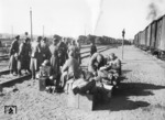 Währen diese Soldaten die kurze Pause in Bobrinskaja genießen, bläst im Hintergund das Sicherheitsventil einer 52er ab. Daneben steht ein Panzertransport mit einem italienischen Schlußwagen. (1943) <i>Foto: RVM (Hollnagel)</i>