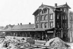 Blick auf das Empfangsgebäude des Bahnhofs Rendsburg. Dieses entstand, nachdem 1845 die rund 34 Kilometer lange, von regionalen Interessenten finanzierte Strecke der Rendsburg-Neumünsterschen Eisenbahn-Gesellschaft zwischen Neumünster und dem damals als Rendsburg-Glacis bezeichneten Bahnhof als Jütlandlinie eröffnet worden. 1904 wurde die Strecke nach Kiel eröffnet, 1910 die Strecke nach Husum, womit der Bahnhof auch erweitert wurde. An der Hafenbahn lag seit 1901 der Übergabebahnhof zur Rendsburger Kreisbahn, die Kreisbahn führte auch den Betrieb auf den vierschienigen Gleisen am Kanalhafen. Personen mussten den knapp einen Kilometer langen Weg zwischen Bahnhof und Rendsburger Kreisbahnhof allerdings zu Fuß zurücklegen. Umfangreiche Veränderungen gab es durch den Bau der Rendsburger Hochbrücke 1913. Die Lage des Bahnhofes blieb erhalten, nur die Ausfahrt Richtung Süden änderte sich. 1957 stellte die Kreisbahn ihren Betrieb ein, der Kanalhafen wurde noch bis 1992 bedient. Der Personenverkehr auf der Strecke nach Husum wurde 1974 eingestellt. Das Bahnhofsensemble ist mit einigen Fassadenerneuerungen bis heute erhalten geblieben. (1912) <i>Foto: Slg. Thorsten Eichhorn</i>
