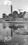 Eine Werkbahn vor unbekannter Industriekulisse im Ruhrgebiet. Möglicherweise handelt es sich um die Sinteranlage der August-Thyssen-Hütte im Duisburger Stadtteil Alsum. In einer Sinteranlage werden feinkörnige Eisenerze zusammen mit Koks und Zuschlagstoffen durch Erhitzen zu einem stückigen, porösen Material (dem sogenannten Sinter) gebacken. Das Sintern ist letztlich das Zusammenbringen von Ausgangsstoffen, welche sich auf andere Weise nur sehr schwer oder gar nicht zu einem neuen Werkstoff verbinden lassen. Ziel des Sinterns in der Eisenmetallurgie ist es, nicht sofort einsatzfähige Feinerze und Konzentrate dem Hochofenprozess zuzuführen. (1955) <i>Foto: Jürgen Hagemann</i>