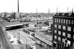 Eine P 8 verlässt den Düsseldorfer Hauptbahnhof in Richtung Wuppertal und fährt gerade über die Kölner Brücke in der nördlichen Bahnhofsausfahrt. Dahinter wird der Zug nach Osten abbiegen und die Ferngleise nach Duisburg überqueren. Auf dem Hof der Hauptpost (rechts unten) sieht man eine größere Zahl von sog. "Weber-Behältern" stehen. Durch Einsatz von Behältern sollte eine Beschleunigung der Paketbeförderung sowie die Vereinfachung der Arbeitsvorgänge in den großen Paketumschlagstellen erfolgen. Es galt, die Pakete – analog den Briefsendungen – frühzeitig zu Lade- und Transporteinheiten zusammenzufassen und die geschlossene Einheit möglichst lange aufrechtzuerhalten. Die Behälter mussten sowohl auf Kraftwagen als auch auf Schienenfahrzeuge verladen werden können und so eine Kombination von Kraftwagen und Schiene ermöglichen. Das Mitte 1951 eingeführte System galt als sehr erfolgreich, weil es tatsächlich ein mehrmaliges Umverteilen der einzelnen Sendungen ersparte, außerdem verminderte es Beschädigungen und Verlust der Pakete. Benannt wurde es nach seinem Erfinder, dem Oberpostrat Weber der Oberpostdirektion Köln. (06.1960) <i>Foto: Ernst Winter</i>