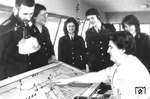 Angehende Fahrdienstleiter(innen) bei der Deutschen Reichsbahn schauen einer erfahrenen Kollegin auf einem nicht näher bezeichneten Rangierstellwerk über die Schulter. Das Unterrichtsziel ergab sich aus dem § 3 (1) der DR-Fahrdienstvorschrift: "Alle Eisenbahner müssen sich  bewusst sein, dass Leben und Gesundheit der Reisenden wie der Eisenbahner selbst, von der sicheren Führung des Eisenbahnbetriebes abhängen und das die Sicherheit des Betriebes schon durch geringfügige Verstöße, gegen die zu seiner Handhabung erlassenen Vorschriften gefährdet werden kann. Mit vereinten Kräften müssen sie danach streben, Unregelmäßigkeiten hintanzuhalten." Dies fand auch seinen Ausdruck im vorschriftsmäßigem Tragen der Uniform. (1973) <i>Foto: Historische Sammlung der Deutschen Bahn AG (Carl-Ernst Zimmer) </i>