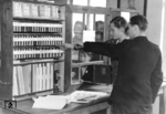 Ausbildung in einer Fahrkartenausgabe in einem Bahnhof der DDR-Reichsbahn mit einem Fahrkartenschrank, dessen Inhalt nach seinem Erfinder auch "Edmonsonschen Fahrkarten" genannt wurde. Thomas Edmondson stellte um 1836 die ersten Fahrkarten aus Karton her, die durch eine einfache Lochung unauslöschbar entwertet werden konnten.  (09.1952) <i>Foto: Slg. Erich Preuß</i>
