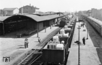 Der thüringische Bahnhof Gotha liegt an der Bahnstrecke Eisenach - Erfurt. Weiterhin zweigen hier die Strecken nach Gräfenroda sowie nach Leinefelde ab. Der Westflügel und Mittelteil des 1847 erbauten Bahnhofs wurde bei Luftangriffen im Zweiten Weltkrieg zerstört, während Ostflügel und Eingangsbereich erhalten blieben. Dieser Zustand ist bis heute so anzutreffen. Am Hausbahnsteig steht wohl eine pr. G 12, die als Schlusslok an einem Personenzug angehängt wurde. Bei dem Ladegut in dem O-Wagenzug handelt sich um Saatgutreiniger K 212 der Firma Petkus aus Wutha, die heute noch in osteuropäischen Ländern anzutreffen sind. (06.1965) <i>Foto: Historische Sammlung der Deutschen Bahn AG</i>
