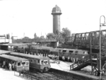 Der S-Bahnhof Ostkreuz ist der am meisten frequentierte Nahverkehrs-Umsteigebahnhof in Berlin. Hier kreuzten ursprünglich die Schlesische Bahn (Berlin Schles Bf—Frankfurt/Oder—Breslau) und die Preußische Ostbahn (Berlin Ostbf—Küstrin—Königsberg/Pr) auf der unteren Ebene mit der Berliner Ringbahn auf der oberen Ebene. Heute steigen hier täglich rund 100.000 Menschen auf neun Linien ein, aus oder um. Auf dem Foto fährt V 180 006 auf den Ferngleisen zum Ostbahnhof, am Bahnsteig D steht vorne ein S-Bahnzug der Bauart Stadtbahn zur Fahrt nach Strausberg (Zuggruppe E). Dahinter ist ein zweiter S-Bahnzug der Bauart ET 167 mit elektrischer Kupplung am Bahnsteig E aus Erkner nach Berlin Friedrichstraße (Zuggruppe B) angekommen. Die ganze Szene überragt der markante 59 m hohe Wassertum.  (1964) <i>Foto: ZBDR</i>