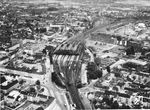 Luftbildaufnahme auf die Anlagen von M Gladbach Hbf mit der dominierenden Bahnhofshalle, gesehen von Süden aus. Die Gleise von unten erreichen den Hauptbahnhof aus Richtung Rheydt. Oben verzeigen sich die Gleise geradeaus nach Viersen und rechts nach Neuß. Dazwischen liegt das Bahnbetriebswerk mit dem einstmals 28-ständigen Ringlokschuppen. Erst zum Fahrplanwechsel am 26. Mai 1963 wurde die bahnamtliche Schreibweise von M Gladbach in Mönchengladbach geändert.  (1960) <i>Foto: BD Wuppertal</i>