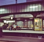 Fahrgäste warten um 20.20 Uhr auf den nächsten Zug in Dortmund Hbf. Ein kleines Detail am Rande ist die Telefonzelle der damaligen Deutschen Bundespost. Durch den Mobilfunk wurden sie immer unwirtschaftlicher und sind heute aus dem Ortsbild verschwunden. Während es 2007 noch 110.000 Telefonzellen in Deutschland gab, waren es 2015 gerade noch 27.000. Seit Ende Januar 2023 sind sie offiziell abgeschaltet und die Münz- sowie Kartenzahlungen nicht mehr möglich. (28.04.1975) <i>Foto: Johannes Glöckner</i>