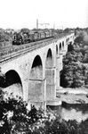 Ein von Kohlfurt kommender, mit einer P 8 bespannter Personenzug überquert das Neißeviadukt zwischen den Bahnhöfen Görlitz-Moys (heute Zgolzelec) und Görlitz. Das 475 Meter lange Viadukt gehört zu den größten und ältesten Eisenbahnbrücken in Deutschland. Eröffnet wurde es 1847 mit der Eisenbahnstrecke zwischen Görlitz und Kohlfurt als Teil der damaligen Bahnverbindung zwischen der sächsischen Hauptstadt Dresden und der schlesischen Provinzhauptstadt Breslau. Am Ende des Zweiten Weltkriegs wurden die höchsten Bögen gesprengt und in den 1950er Jahren unter polnischer Leitung wieder aufgebaut. Die wiedererrichteten Bögen unterscheiden sich heute noch deutlich in ihrer Farbe vom älteren Teil des Viadukts. Seit Mai 1957 können Züge an dieser Stelle wieder die Lausitzer Neiße und somit nun auch die deutsch-polnische Grenze überqueren. (1936) <i>Foto: RVM</i>