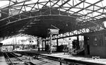 Blick in den Bahnhof Wuppertal-Oberbarmen, der mit Eröffnung der Bahnstrecke am 9. Oktober 1847 (Elberfeld (-Döppersberg) - Schwelm) eigentlich (Barmen-)Rittershausen hieß. Die Bezeichnung "Oberbarmen" erhielt er erst nach der Gründung der Stadt Wuppertal (1929) im September 1930. Obwohl im Zweiten Weltkrieg stark beschädigt, überlebt die Bahnhofshalle den Krieg. Der ganze Bahnhof wirkte aber bis zu seinem kompletten Neubau im Jahr 1988 als Provisiorium, das auch durch den Zustand der Halle unterstrichen wird. Interessant ist auch das Zwischensignal in Gleis 3, das zur besseren Erkennbarkeit eine Kontrasttafel erhalten hatte.  (1954) <i>Foto: Carl Bellingrodt</i>