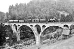 Über das 152 m lange Holdereck-Viadukt rollt 75 1101 (Bw Karlsruhe Pbf) mit P 3926 nach Freudenstadt bei Forbach-Gausbach durch das Murgtal. Die 1914 eröffnete Brücke wurde nur 31 Jahre alt, da sie die Deutsche Wehrmacht noch im April 1945 völlig sinnlos sprengte. Heute überspannt an der Stelle, an der einst das steinerne Viadukt stand, eine 144 m lange Stahlbrücke die Murg. Es handelt sich um ein Provisorium, das im Spätsommer 1947 errichtet wurde. Damit steht das Provisorium mittlerweile deutlich länger als die Vorgängerin. (20.06.1934) <i>Foto: DLA Darmstadt (Bellingrodt)</i>