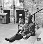 Ein Gepäckträger wartet im (kriegszerstörten) Anhalter Bahnhof von Berlin auf Kundschaft. Vor 1945 war der Anhalter Bahnhof der bedeutendste Berliner Fernbahnhof für alle Zugverbindungen in Richtung Süden. Nachdem das Bahnhofsgebäude am 3. Februar 1945 durch Luftangriffe der Alliierten schwer beschädigt worden und ausgebrannt war, wurde es nur enttrümmert und notdürftig wieder betriebsfähig gemacht. Ab dem 18. Mai 1952 wurde der Betrieb auf dem Anhalter Bahnhof endgültig eingestellt und die Anlagen dem Verfall preisgegeben. Nach der Sprengung der Halle im Jahr 1959, blieb nur noch der Portikus mit einem Teil der überdachten gemauerten Vorfahrt stehen.  (1948) <i>Foto: Henry Ries</i>