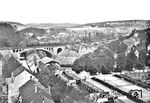 Blick von der Evangelischen Kirche in Elberfeld-Sonnborn auf eine P 8, die gerade über die Wupperbrücke am Zoo westwärts fährt. Unten die Schwebebahnstation "Am Zoo", mit einem damals noch hölzernen Übergang über die Wupper. Rechts die Tennisanlagen des (nicht mehr sichtbaren) Stadions, oben rechts die Anlagen der Bayer-Werke und der Blick auf den fast noch unbebauten Nützenberg. (1928) <i>Foto: Rbd Elberfeld</i>