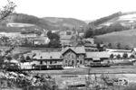 Blick auf den Bahnhof Niederseßmar mit seinem regionstypischen Gebäudekomplex. Gut zu erkennen ist auch, dass der Ort auch altes Industriegebiet ist. Die Aufnahme stammt von vor 1915, denn von der in diesem Jahr in Betrieb genommenen Kleinbahn zwischen Gummersbach und Derschlag ist noch nichts sehen. Beim Bahnhof in Niederseßmar gab es ein Verbindungsgleis zur normalspurigen Privatbahn. Mit Stilllegung des Abschnitts Dieringhausen – Olpe wurde der Bahnhof funktionslos. Auf dem Gebiet von Niederseßmar sind nur Trassenreste der Strecke vorhanden, so durchschneidet heute ein amerikanisches Fastfood-Restaurant die seit 2013 gleislose Trasse. Das Empfangsgebäude existiert allerdings noch. (1910) <i>Foto: Slg. Dr. Hans-Jürgen Vorsteher</i>