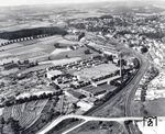 Eine Luftaufnahme von den Lenneper Bahnanlagen. Oben rechts ist der Bahnhof mit dem Empfangsgebäude samt Türmchen und den hellen Seiten- und Kopfbahnsteigen zu erkennen. Am rechten südlichen Ende der Kopfgleise gibt es eine Freifläche, wo früher das Bw Lennep (alter Schuppen) lag. Links davor liegen die Abstellanlagen mit Güterschuppen und weiten Freiladebereiche. Rechts vom Bahnhof ist der etwas tieferliegende Altstadtkern von Lennep mit seiner engen Rundbebauung und den beiden Kirchen in Marktnähe auszumachen. Im vorderen Bereich dominieren die Anlagen der Firma Wülfing. Gut zu erkennen sind daneben die zweigleisigen Strecken nach Remscheid Hbf und rechts nach Bergisch Born. Die Straßenüberführung an der Verzweigung befindet sich im Bereich Trecknase/Tenter Weg. Rechts mittig am Bildrand bei den Häuserzeilen ist der Trassenabzweig der ehemaligen Bahn nach Krebsöge auszumachen. Die Strecke am oberen Bildrand führt aus dem Bahnhof heraus nach Rd-Lüttringhausen, wobei das helle Band der Autobahn A 1 unterquert wird. An der Autobahn liegen die Häuser vom Weiler Garschagen, nicht weit entfernt vom Lüttringhauser Wasserturm. Am Rand der großen Waldfläche ist gerade noch das Bw Lennep auszumachen, wobei der Lokschuppen ins Auge fällt. Etwas darüber, links der Trasse, ist das Betriebswagenwerk zu erkennen.  (1959) <i>Foto: Wilfried Sieberg</i>
