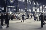Blick in den Querbahnsteig in Frankfurt Hbf mit seinen fünf Stahl- und Glashallen, die auf einer Länge von 186 Metern die Bahnsteige überdachen. Die drei größeren Hallen haben eine Breite von 56 Metern und eine Höhe von 28 Metern, die beiden äußeren kleinen Hallen eine Breite von 31 Metern und eine Höhe von 20 Metern. Über die gesamte Breite der Hallen erstreckt sich der Querbahnsteig, der Zugang zu den 24 oberirdischen Hauptgleisen in den Hallen ermöglicht. Rechts steht eine Frankfurter E 10.3, die mit dem E 539 angekommen ist. Der schnellzugmäßige Wagenpark lief dann um 16.47 Uhr als N 4934 nach Darmstadt mit einer E 41. Rechts ist der N 3785 in den Vogelsberg nach Gedern angeschrieben, der um 16.59 Uhr mit einer 78er fuhr. Links steht eine E 41, die mit dem P 4820 aus Offenbach angekommen ist. (1964) <i>Foto: Reinhold Palm</i>