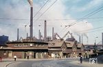 Der Bahnhof Völklingen wurde im Zuge des Baus der Saarstrecke am 16. Dezember 1858 eröffnet. 1860 wurde das erste Empfangsgebäude errichtet, das sich östlich des heutigen Gebäudes befand. Im Deutsch-Französischen Krieg war der Bahnhof Ziel französischen Artillerie-Feuers, das den Bahnbetrieb unterbrechen sollte. 1893 wurde das zu klein gewordene Bahnhofsgebäude durch den hier sichtbaren Bahnhof ersetzt. Zur Blütezeit der nahegelegenen Völklinger Hütte diente der Bahnhof als wichtiger Verkehrsknoten für Hüttenarbeiter und Rohstoffe. 1992 wurde der Neubau eines Empfangsgebäudes unmittelbar neben dem bestehenden eingeweiht, nachdem bereits seit 1975 über einen Neubau diskutiert worden war. Der alte Bahnhof wurde unter Denkmalschutz gestellt. Von 1909 bis 1959 verkehrte auch die Straßenbahn Völklingen zum Bahnhof. Für Sauberkeit wird auch gesorgt, ob aber angesichts des rotbraunen Staubes von der Hütte die einsame Reinigungsaktion (rechts) wirklich erfolgreich war, mag dahingestellt sein. (21.06.1960) <i>Foto: Carl Bellingrodt</i>