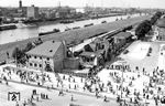 Das im Zweiten Weltkrieg zerstörte Empfangsgebäude des Bahnhofs Mannheim-Neckarstadt wurde bis auf die Grundmauern bereits abgetragen, der Neubau startete jedoch erst zwei Jahre später. Für den Berufsverkehr steht eine lange Wagenreihe von Behelfspersonenwagen der Bauart MCi-43 bereit. Gut zu erkennen ist hier die Lage des Bahnhofs entlang des Neckardammes. Das Empfangsgebäude lag schräg gegenüber dem Bahnhof Mannheim der OEG im Winkel von Dammstraße und Kurpfalzbrücke, seitlich des alten Messeplatzes. Eine Gleisverbindung zum Hauptbahnhof Mannheim gab es zunächst nicht.  (1950) <i>Foto: BD Mainz, Slg. W. Löckel</i>
