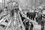 Abriss der Bahnübergangsanlagen an der Rohrbacher Straße in Heidelberg unter großer Anteilnahme der Bevölkerung. Mit zunehmendem Straßenverkehr erwies sich insbesondere der 1862 beim Bau der Odenwaldbahn entstandene Bahnübergang der Rohrbacher Straße am heutigen Adenauerplatz als störend. Schon Ende 1949 passierten bereits 10.800 Fahrzeuge den Übergang, der täglich drei bis vier Stunden geschlossen war! Für Fußgänger stand seit 1893 eine Unterführung zur Verfügung. Auch Linien der Heidelberger Straßenbahn waren durch den Bahnübergang teils stark verspätet, daher mussten die Fahrgäste den Übergang ab 1948 zu Fuß passieren, da die Straßenbahnlinien beiderseits des Bahnübergangs endeten. Der Bahnübergang galt als einer der Hauptgründe für die Bahnhofsverlegung. (1955) <i>Foto: BD Karlsruhe</i>