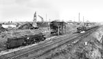 Blick auf die weitläufigen Anlagen des Bw Stralsund. Während 03 0010 mit D 715 (Putbus – Leipzig) gerade den Bahnhof Stralsund verlässt, rangiert im Vordergrund 03 0019 am Kohlenhochbunker. Eine weitere Lok steht unter der Ölbunkeranlage und ergänzt ihre Voräte. 03 0010 hat inzwischen den Giesl-Ejektor und die Gegendruckbremse eingebüßt.  (25.09.1975) <i>Foto: Michael Malke</i>